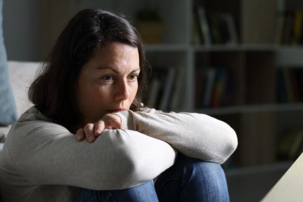 A woman sits on the ground as she considers the physical signs of meth use in adults and the symptoms of meth addiction