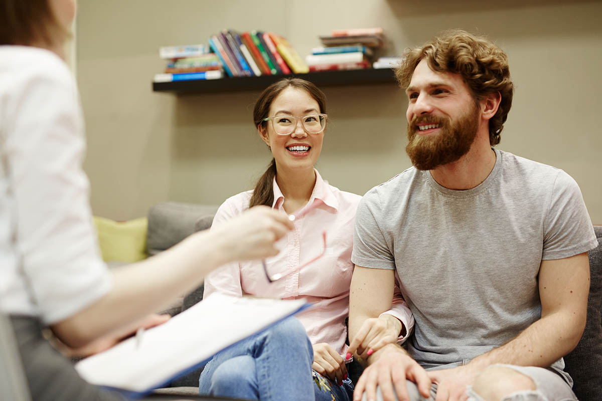 What is Family Therapy And Who is it For Couple smiling, sitting on couch, during family therapy
