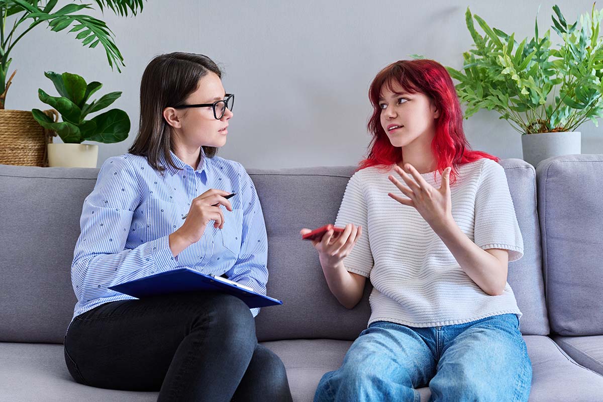 25 Red Flags in Teenage Behavior Teen and therapist sit on couch and discuss red flags in teenage behavior
