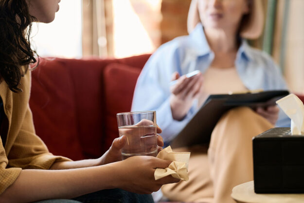 The Anger Iceberg and Processing Emotions Woman holds glass of water as the discusses anger icebergs with her therapist